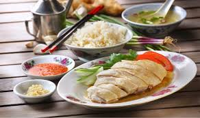 A plate of chicken rice with some chilli sauce and ginger on the side.